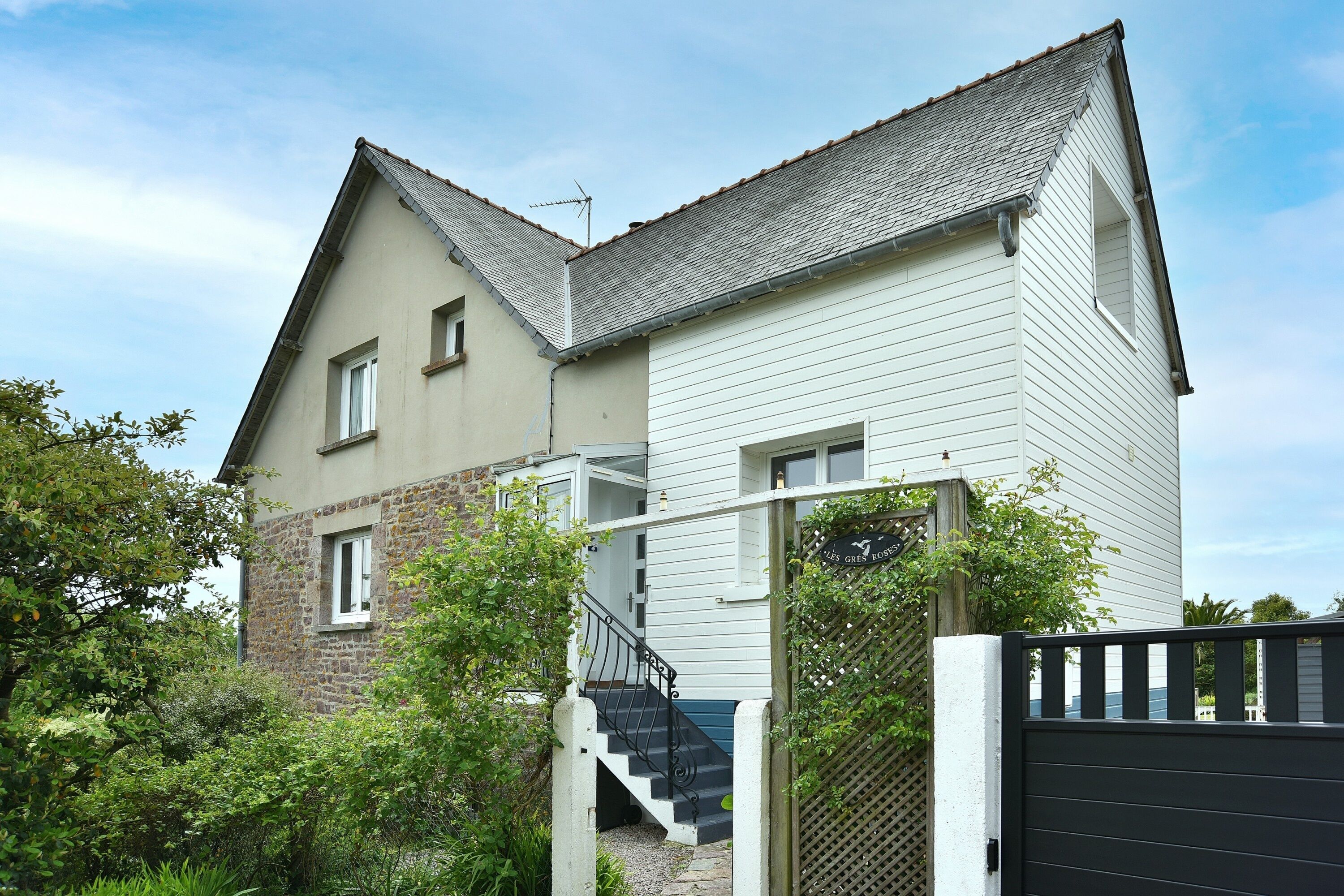 A two-story house with a stone facade, a white upper level, and a black gate.