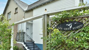 A building with a sign reading 'LES GREES ROSES' and a wooden fence with climbing plants. - Les Grès roses - Appartement cosy sur la côte (Fréhel)