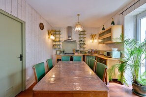 Een keuken met een houten tafel, groene stoelen, een fornuis en planken met flessen.