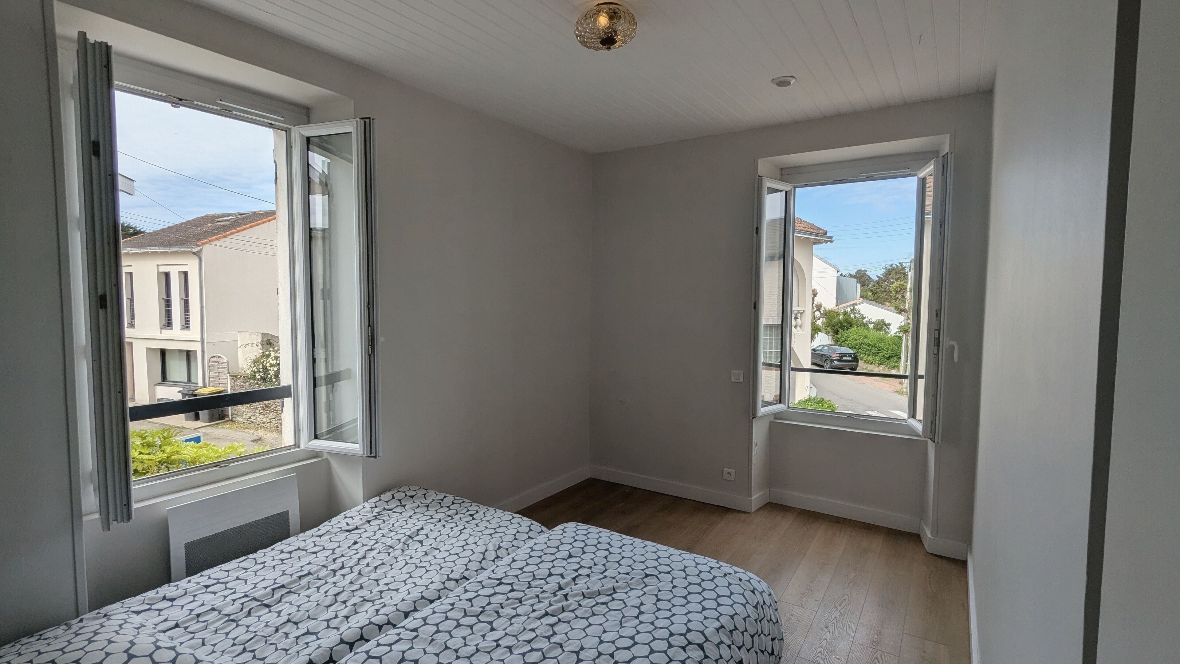 Ein Schlafzimmer mit einem Bett, zwei Fenstern und Blick auf die Straße.