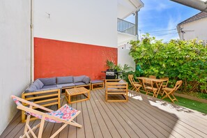 Een houten terras met tuinmeubilair, een barbecue en een rode muur.