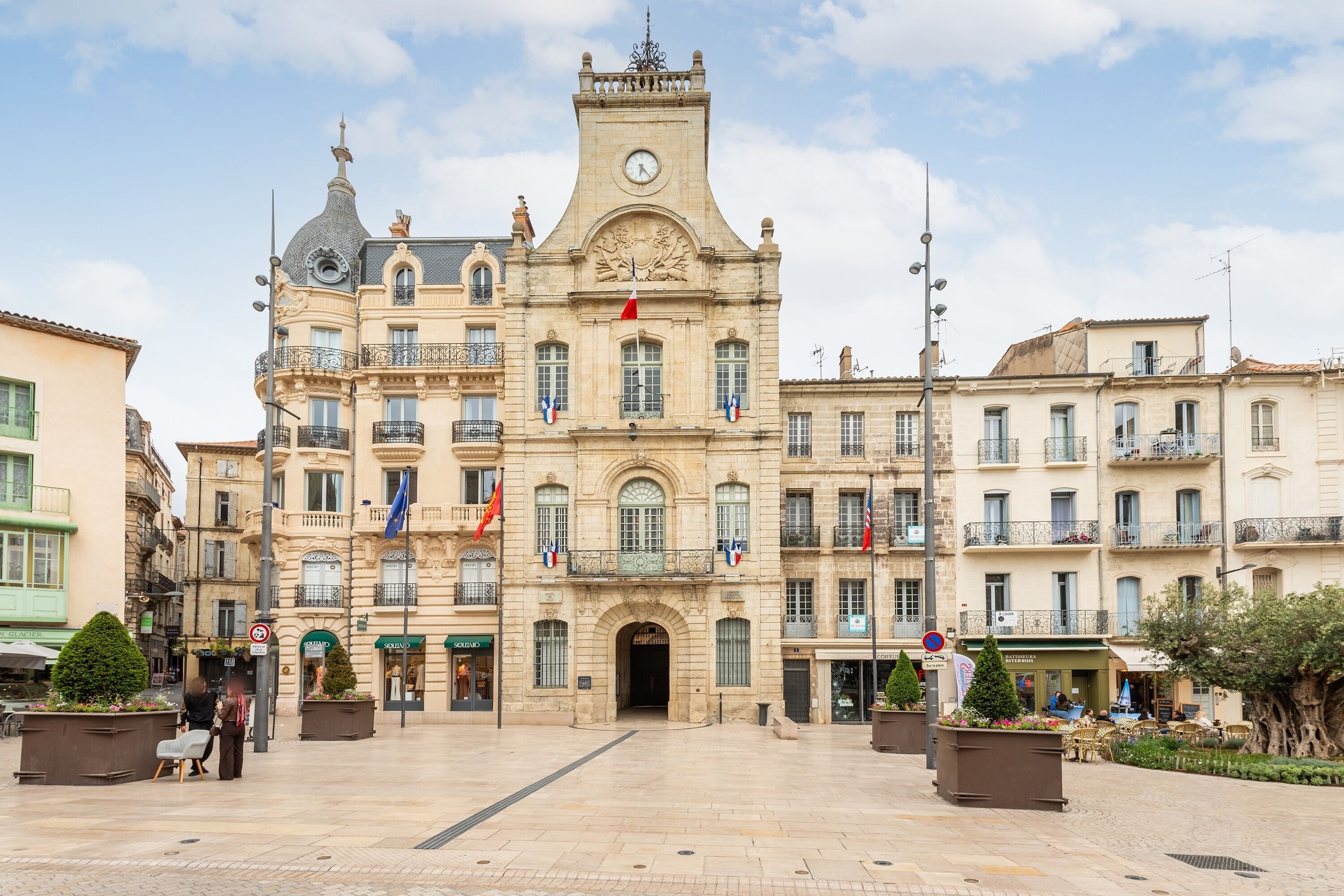 A historic building with a clock tower, multiple flags, and a central entrance.