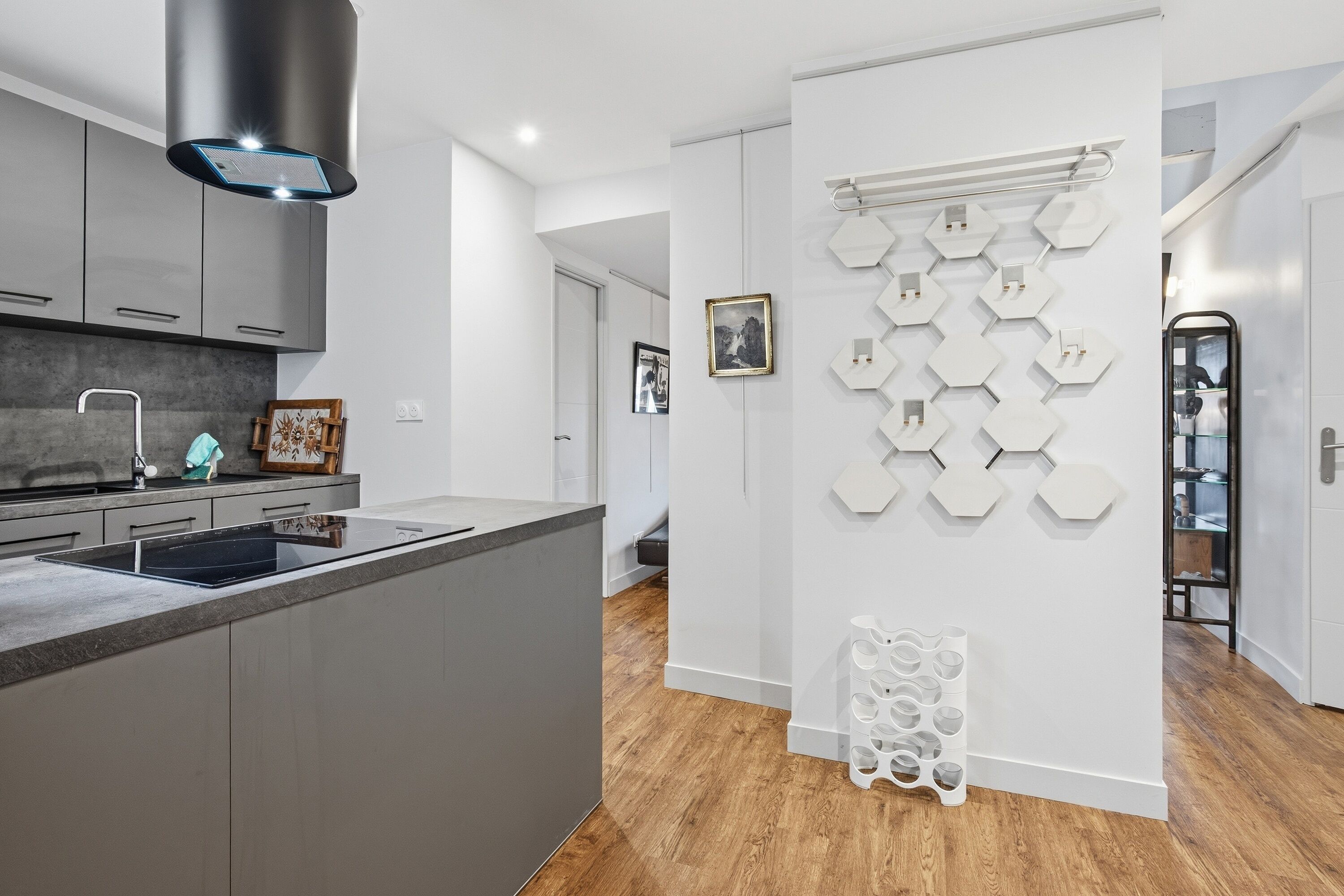 A modern kitchen with grey cabinets, a stainless steel range hood, and a hexagonal wall decoration.