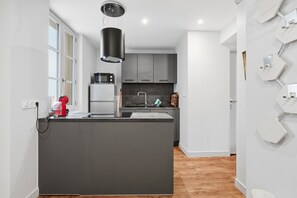 A modern kitchen with a central island, grey cabinets, and a black pendant light. - Le Dôme - Au cœur du centre-ville de Béziers (Béziers)