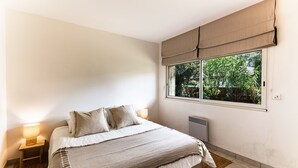 A bedroom with a bed, bedside lamps, a window with a view of greenery, and a radiator. - La Villa Amarra - À 1 km du Golf de Moliets-et-Maa (Moliets-et-Maa)