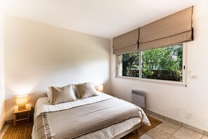 Ein Schlafzimmer mit Bett, Nachttischlampen, einem Fenster mit Blick auf Grünflächen und einer Heizung.