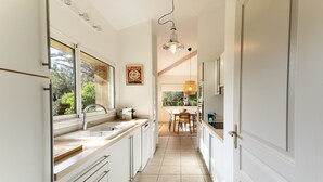 A narrow kitchen with white cabinets, a window, and a pendant light. - La Villa Amarra - À 1 km du Golf de Moliets-et-Maa (Moliets-et-Maa)