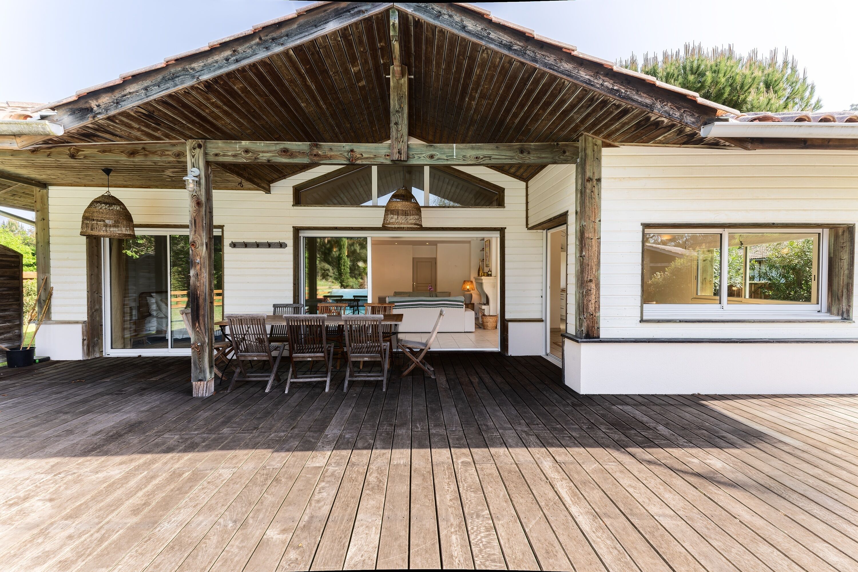 A wooden deck with a covered patio area, a dining table with chairs, and a view of the interior through a glass door.