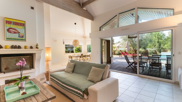 A spacious living area with a sofa, a fireplace, a dining table, and a patio with outdoor furniture. - La Villa Amarra - À 1 km du Golf de Moliets-et-Maa (Moliets-et-Maa)