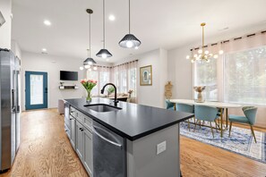 A modern kitchen with a central island, stainless steel appliances, pendant lighting, and a dining area with a table and chairs. - 6 Min to DT! Luxe Home! Karaoke Stage! (Nashville)