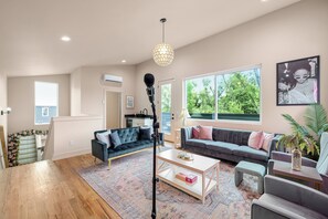 A spacious living room with a large window, a sofa, a coffee table, and a microphone stand. - 6 Min to DT! Luxe Home! Karaoke Stage! (Nashville)