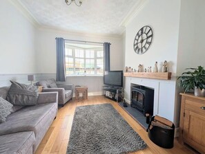 A living room with a fireplace, a television, a sofa, and a large window with curtains.