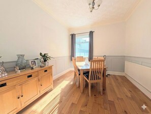 A dining area with a wooden table and chairs, a cabinet with decorative items, and a window with curtains.