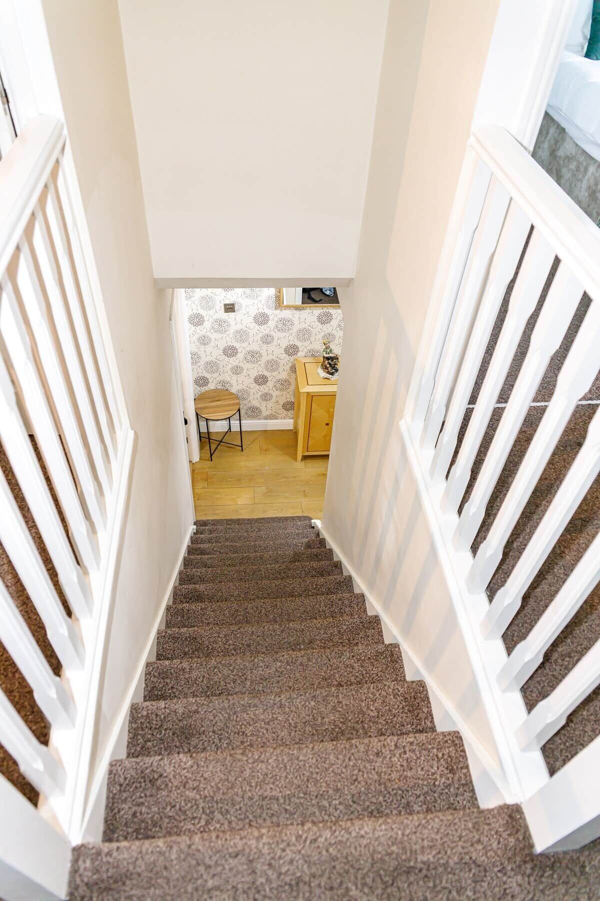 A staircase with white railings leading to a room with a wooden floor and a small table.