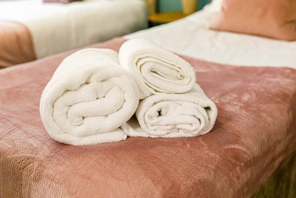 Een bed met een roze deken en opgerolde witte handdoeken.