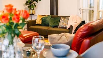 A living room with a sofa, cushions, a table with a bowl and wine glass, and a plant.
