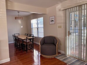 Un comedor con una mesa y sillas de madera, un sillón gris y una ventana con persianas.