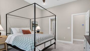 A four-poster bed with a checkered bedspread, two bedside tables with lamps, a wall-mounted painting, and a door leading to another room.