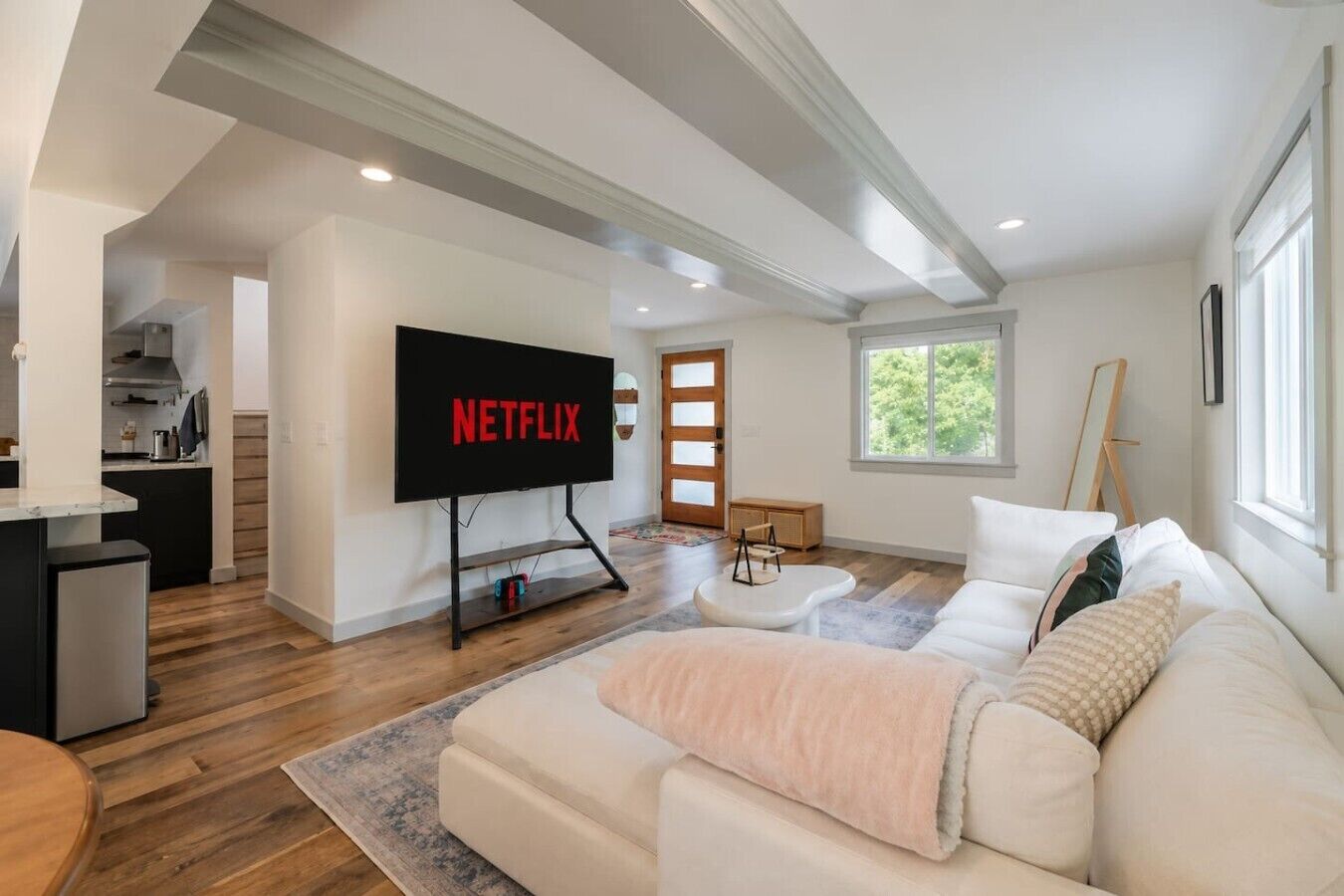 A modern living room with a flat-screen TV, a sofa, a coffee table, and a kitchen area in the background.