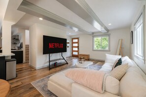 A modern living room with a flat-screen TV, a sofa, a coffee table, and a kitchen area in the background. - 4BR Seattle Stunner | w/ Summer Deck by Green Lake (Seattle)