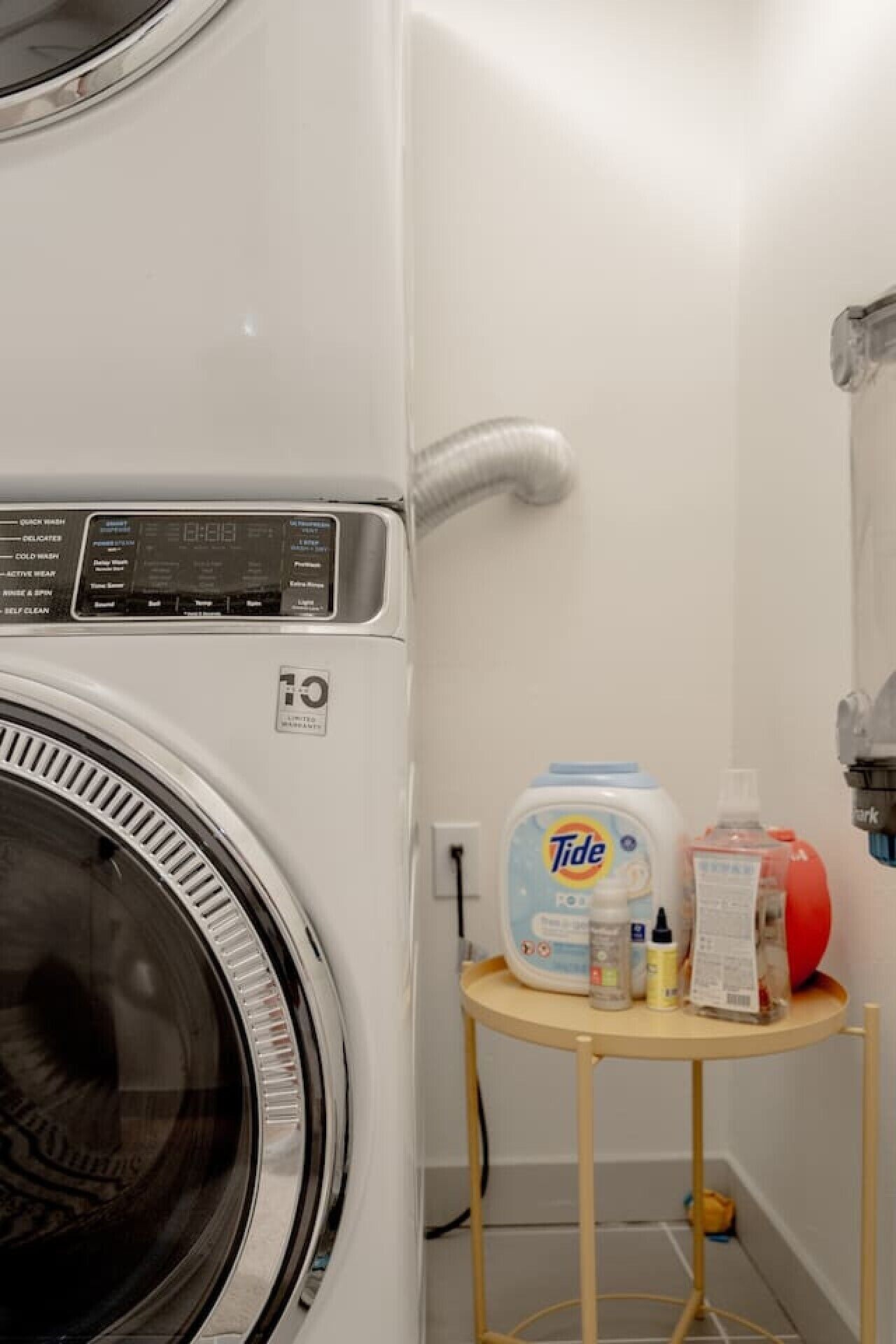 A front-loading washing machine with Tide detergent and other cleaning supplies on a small table.