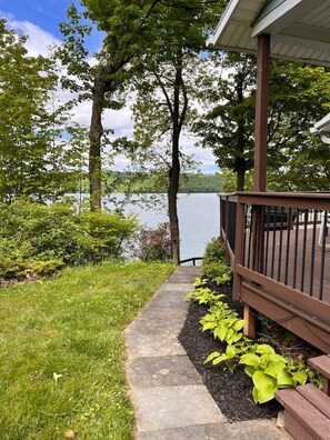 A pathway leading to a wooden deck with a view of a lake and trees. - Owasco Lake Cottage | Lake Front | Dock | Fire Pit (Moravia)
