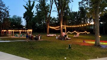 An outdoor event area with tables and chairs, string lights, and trees.