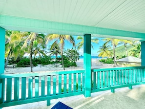 Un espace extérieur abrité, doté d’une balustrade turquoise, de palmiers et offrant une vue sur la plage.