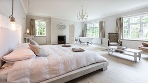 Ein geräumiges Schlafzimmer mit einem großen Bett, einer Sitzecke mit Sessel und Tisch, einer Badewanne und einem Kamin.