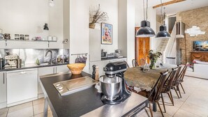 A modern kitchen with a central island, a dining area with a table and chairs, and a staircase leading to an upper level. - Le Jardin Du Chateau (Duras)