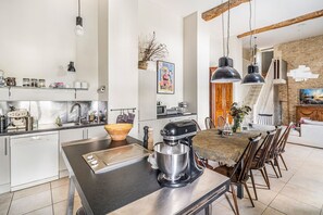 Una cuina moderna amb una illa central, una zona de menjador amb taula i cadires, i una escala que condueix a un nivell superior.
