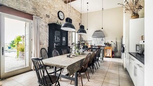 A spacious dining area with a long table, chairs, and pendant lighting. - Le Jardin Du Chateau (Duras)