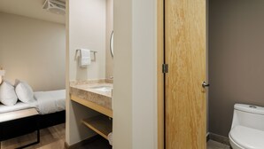 Een hotelkamer met een bed, een badkamer met wastafel en toilet, en een houten deur.