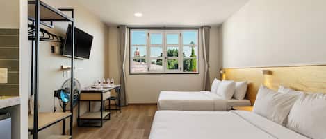 A hotel room with two beds, a desk with a chair, a TV, and a window with a view of a building and trees.