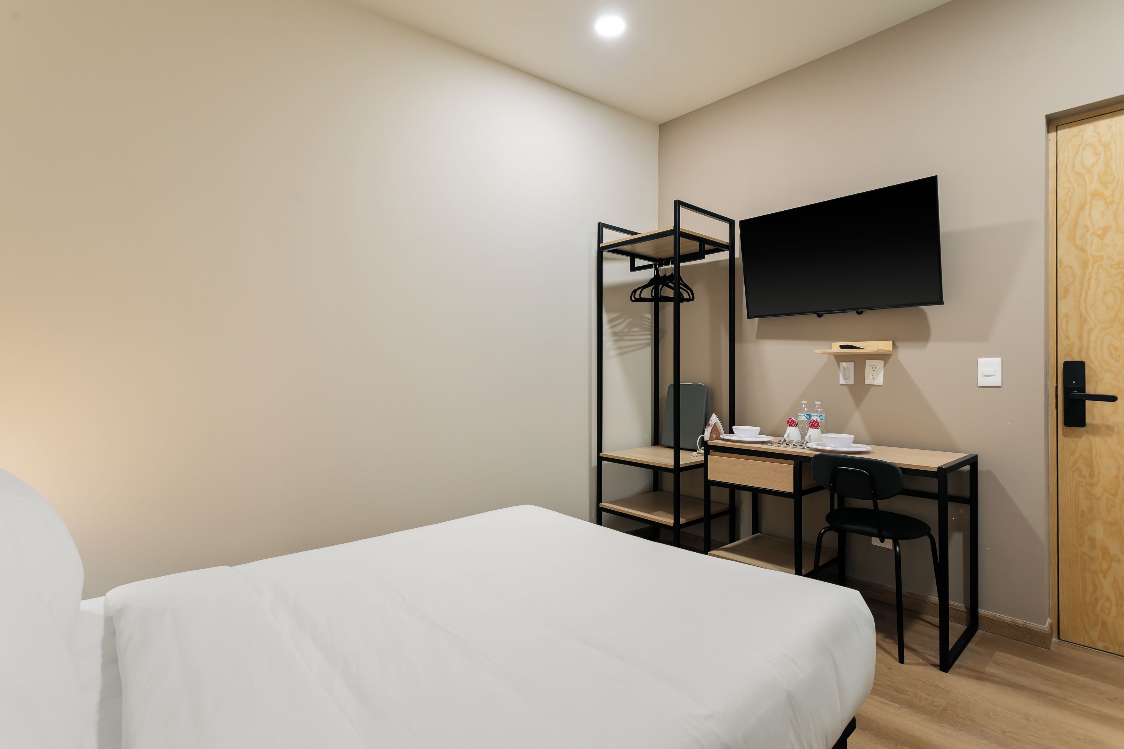 Een hotelkamer met een bed, een bureau, een stoel, een aan de muur bevestigde televisie en een houten deur.