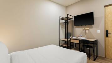 Een hotelkamer met een bed, een bureau, een stoel, een aan de muur bevestigde televisie en een houten deur.