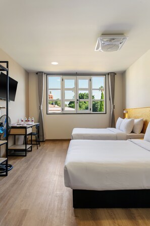 Habitación de hotel con dos camas, un escritorio, una silla, un televisor y una ventana con vistas a zonas verdes y un edificio.