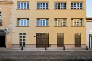 Un edificio con varias ventanas y puertas, una calle empedrada con ladrillos y bolardos.