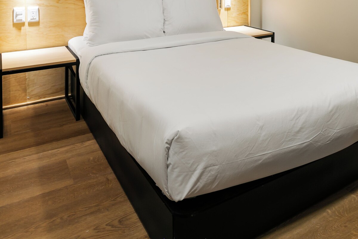 A modern hotel room with a wooden headboard, a large bed with white linens, two bedside tables with lamps, and a ceiling fan.