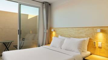 Habitació d'hotel amb un llit gran, una taula de nit, una làmpada penjada a la paret i una porta corredissa de vidre que dona a un balcó.