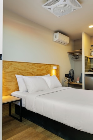 A hotel room with a wooden headboard, a bed with white bedding, a bedside table, a wall-mounted air conditioner, a small fan, and a kitchenette area with a blender and a toaster. - Madero By Homirent (Queretaro)