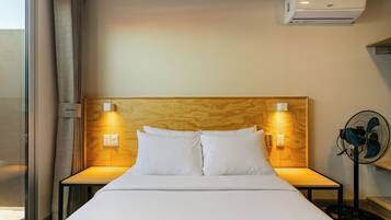 Een hotelkamer met een bed, twee bedlampen, een luchtverkoeler aan de muur en een staande ventilator.