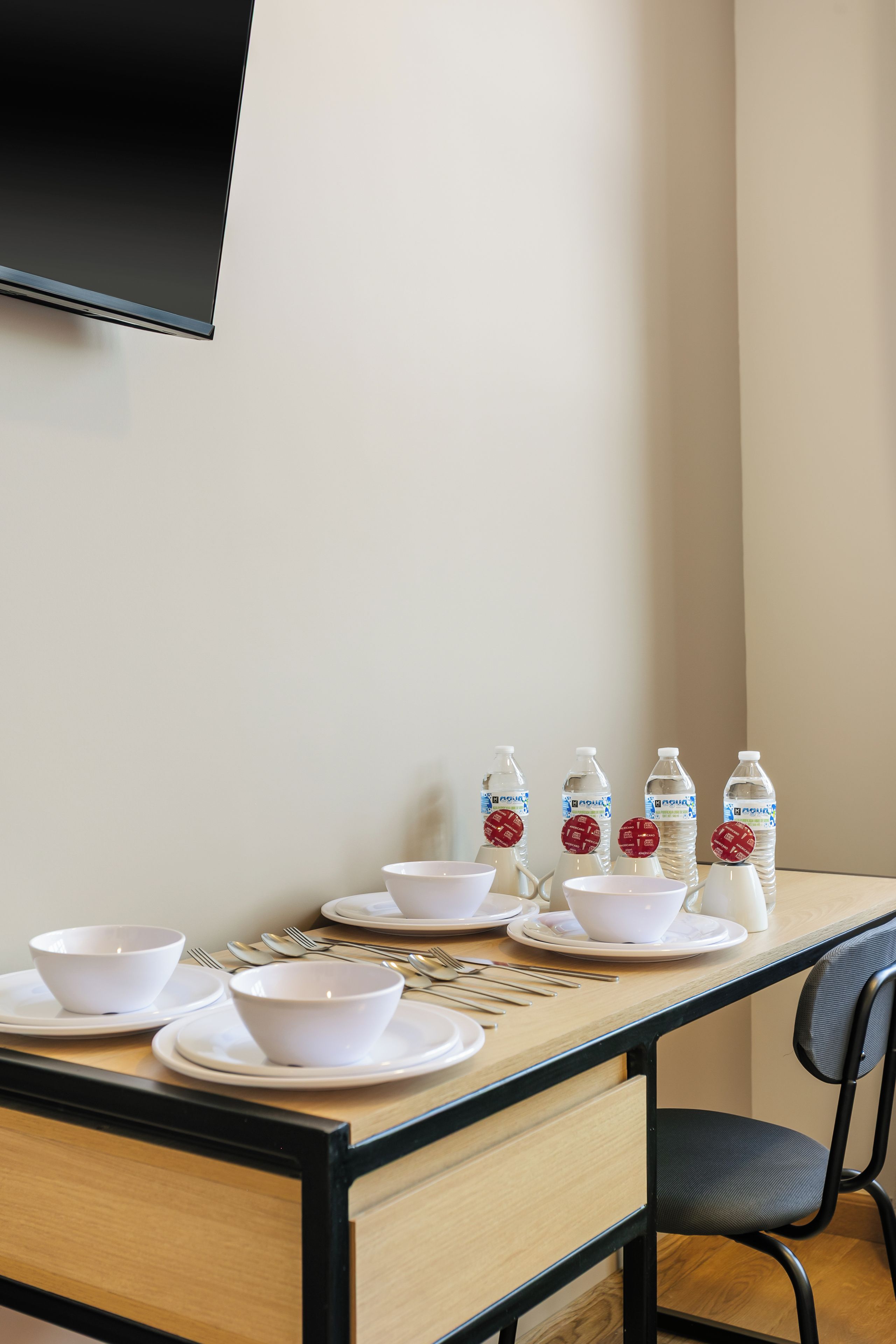 A dining table set with white bowls and plates, accompanied by water bottles and cutlery.
