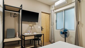 Een hotelkamer met een bed, een bureau met stoel, een televisie, een ventilator en een kledingkast.