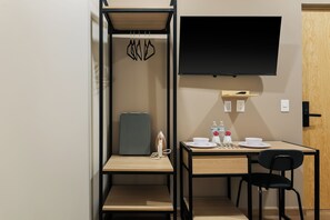 A compact room with a bed, a desk, a chair, a flat-screen TV, and a small shelf with a bottle and a cup. - Madero By Homirent  (Queretaro)