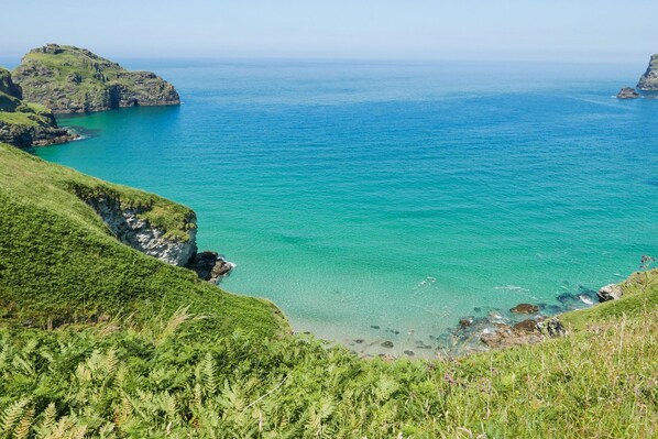 A coastal landscape with cliffs, clear turquoise sea, and lush greenery.