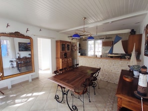 A dining area with a wooden table and chairs, a kitchen with a stone wall, and a large mirror.