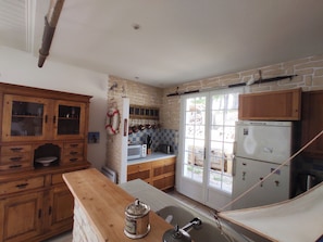 A kitchen with wooden cabinets, a hanging pot rack, a refrigerator, and a window with a view of the outside.