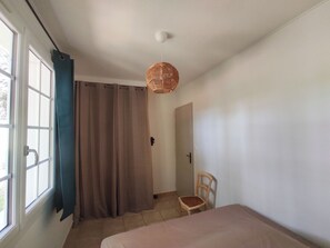 A room with a bed, a chair, a window with curtains, and a hanging light fixture.