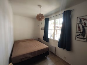 A small, single-bed room with a window, a radiator, and a wall-mounted artwork.